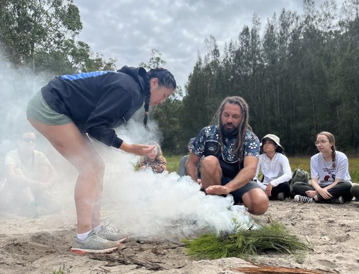 一名学生俯身在冒烟的草地上，这是土著居民焚烧本土植物以驱除恶灵的习俗.